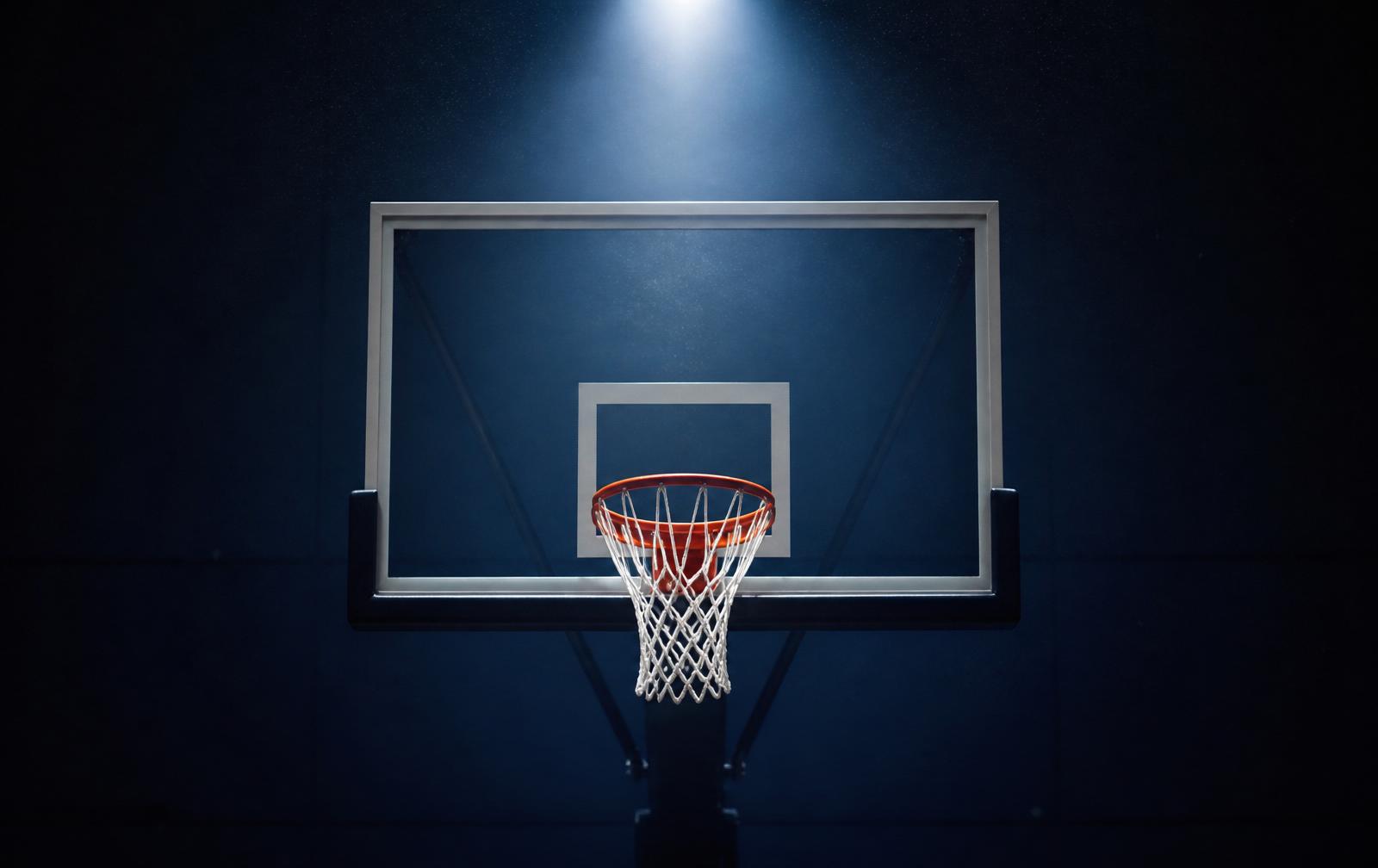 Basketball hoop with fresh white net lit by an overhead spotlight in a dark gym